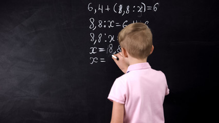 Boy writing on chalkboard math equation, solving exercise, education reform