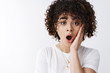 © Cookie Studio - Wow no way, you kidding me. Impressed surprised curly-haired woman learn shocking rumor drop jaw say wow touch cheek thrilled astonished wide eyes camera stunned, white background