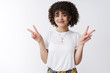© Cookie Studio - Peace everyone. Cute curly-haired queer girl smiling friendly show victory gestures sideways celebrate happy pride standing joyfully upbeat good mood standing white background