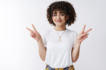 Wall Mural - Peace everyone. Cute curly-haired queer girl smiling friendly show victory gestures sideways celebrate happy pride standing joyfully upbeat good mood standing white background