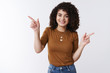 © Cookie Studio - Playful happy smiling silly curly-haired european 20s girl pointing sideways left right showing choices good products laughing friendly suggestion promoting copy space giving direction