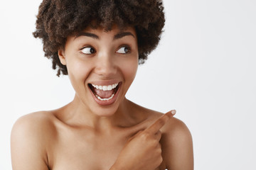 Wall Mural - Cannot hide happiness when it is pure, just like my skin. Portrait of amazed and pleased good-looking african american posing naked over gray wall, pointing and gazing right with joy over grey wall