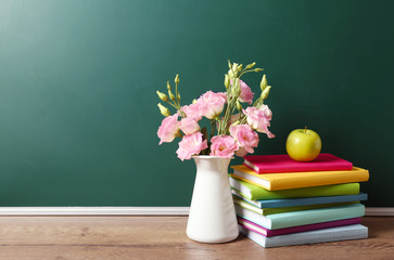 Wall Mural - Vase of flowers, books and apple on wooden table near green chalkboard, space for text. Teacher's day