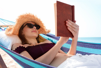 Poster - Young woman reading book in hammock on beach