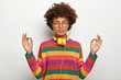 Relaxed beautiful lady with Afro hairstyle meditates indoor, keeps eyes closed, feels satisfied lo listen pleasant music in headphones, wears spectacles, earrings, striped jumper. Body language