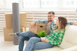 © satura_ - Positive cheerful couple rejoices in moving their new apartment sitting in the living room with their belongings. Concept of housewarming and mortgages for a young family.