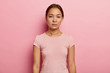 © wayhome.studio  - Photo of serious calm woman with dark hair, dressed in casual wear, looks straightly at camera, has fresh skin, wears piercing in ear, poses against pink background. People, feminity, beauty concept