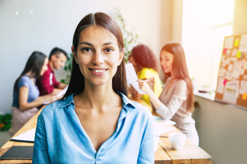 Wall Mural - Attractive confident modern business woman in casual clothes looks at the camera and smiling. Modern start-up business team. Co-workers or students 