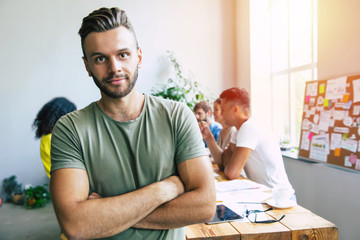 Wall Mural - Handsome young business man in smart casual wear on background of brainstorming modern start up team in office or co-working centre