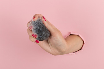 Wall Mural - Girl hand holds a beauty blender for makeup from a hole in a pink background, copy space. Sponge in soapy foam, how to clean.