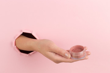 Girl hand holds powder from a hole in a pink background. Makeup artist concept, copy space.