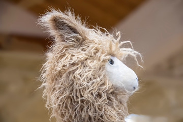 Cute fuzzy toy llama head against light brown background - cropped