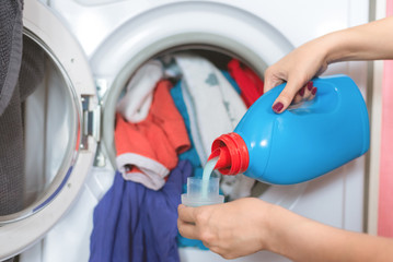 Wall Mural - Woman is holding in hands a liquid laundry detergent on a washing machine background.