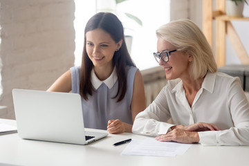 Canvas Print - Smiling female employees work at laptop in office together