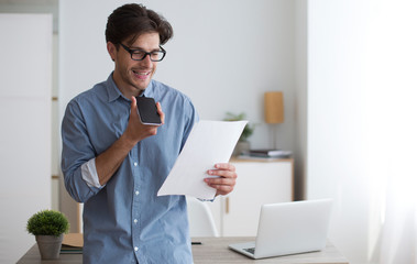 Poster - Business Guy Using Cellphone Voice Assistant Reading Papers In Office