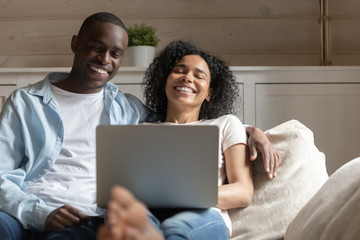 Wall Mural - Happy biracial couple relax laugh using laptop at home