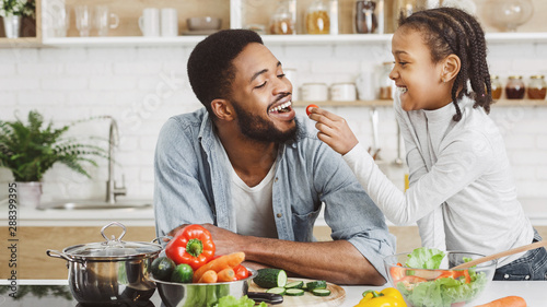 Fotografía Cute african girl giving her dad cherry tomato while cooking