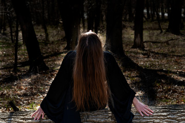 Young Woman with dark long hair in black robes deep in the Forest. Witches. Halloween and Gothic concept. Witchcraft and magic. 