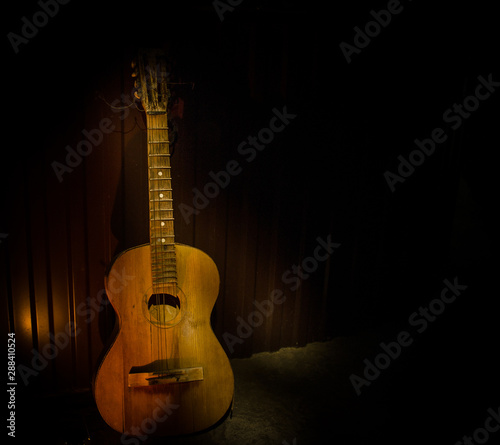 Obraz Dibond An wooden acoustic guitar is against a grunge textured wall. The room is dark with a spotlight for your copyspace.