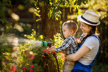 Woman Gardener With Son Watering Garden