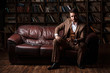 © Ilnur - young successful man in a brown kosmtyum drinks whiskey. bearded businessman sitting in a library on a luxurious leather sofa and drinking cognac