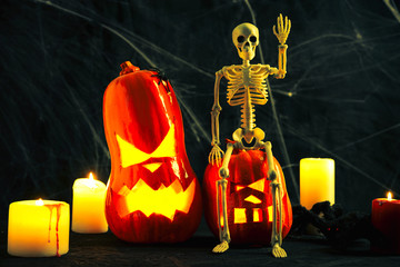 Halloween symbol, two pumpkin Jack lamp with glowing eyes, human skeleton, gloomy and dark atmosphere, stretched web in the background, lighted candles