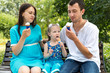 © jonnyslav - Father, mother and daughter sit on bench and eat ice cream. Woman pregnant.