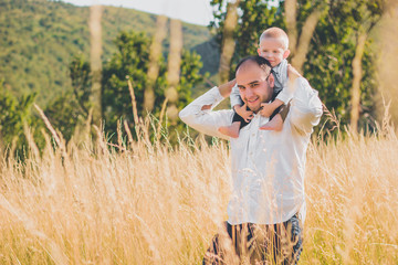 Happy family with kid walking together in wheat field on warm and sunny summer day. Soft focus.