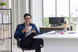 © kurapy - Asian, businessman, In hand holding white coffee mug. front on the desk. there are laptop computer, in the office room.