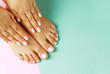 Female hands with white manicure and pedicure on a pink and blue background, top view