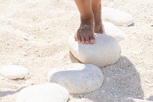 A Closeup View On The Bare Feet Of A Young Child Playing And Standing On White Stones On A Sandy Beach During Summer Vacation, Stepping Stones With Room For Copy.