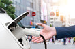 © zapp2photo - EV automotive , Air pollution and reduce greenhouse gas emissions concept. Hand holding and charging Electric car with blur city view background.