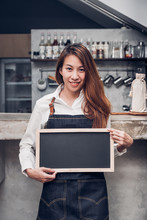 Young Asian Barista Wear Jean Apron Holding Blank Blackboard Coffee Menu At Counter Bar With Smile Face,cafe Service Concept,business Owner Start UpLeave Space For Adding Your Text..
