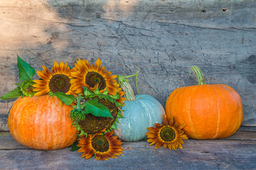 Wall Mural - Beautiful autumn composition: three ripe orange pumpkins and sunflowers on the old wooden background with copy space