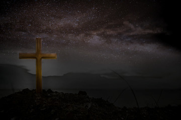 Wall Mural - Cross wooden raised to the glory of God, Jesus Christ. Night light lighting a fire on a background of stones under the stars of the Milky Way.