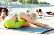 © Дарья Фомина - A big group of people attending yoga classes on a pontoon near the lake.