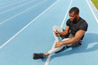 © alfa27 - african attractive sportsman using smart phone while sitting on the running track. full length photo. rest time, free time , spare time. copy space