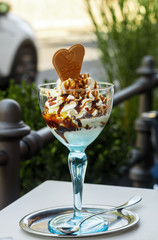 Wall Mural - Dessert of ice cream, whipped cream, walnuts and caramel (maple syrup) in a tall blue glass in a street cafe. Selective focus