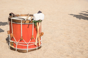 Large red drum in the ethnic style with covered cords, with two types of sticks, is on light sand.