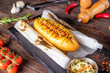 Wall Mural - Hot dog with sausage is located on a wooden board against a dark background, rustic style, horizontal orientation