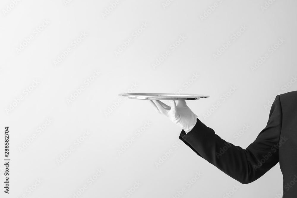 Hand of waiter with empty tray on light background