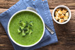 Fresh homemade cream of broccoli soup in bowl garnished with broccoli florets, fresh crispy croutons on the side, photographed overhead (Selective Focus, Focus on the soup)