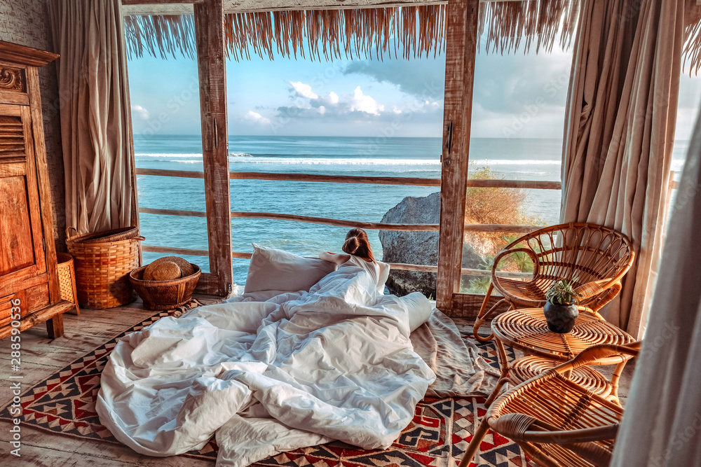 Woman enjoying morning vacations on tropical beach bungalow looking ocean view Relaxing holiday at Uluwatu Bali ,Indonesia - obrazy, fototapety, plakaty 