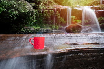 Wall Mural - red cup of coffee with waterfall nature background