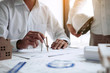 © wutzkoh - Two engineering working together and using compass looking blueprint and analysis with architectural plan on desk.