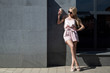 © Денис Бухлаев - beautiful slender european girl blonde in pink tshirt and coat, sunglasses stands near gray concrete wall with glass take away coffee. copy space