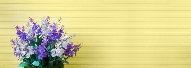 beautiful purple lavender or lilac plastic flower bouquet in pretty vase on stripe textured yellow w