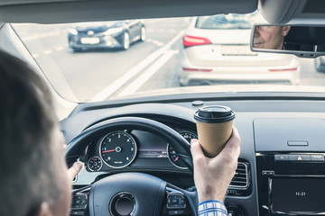 Elderly Businessman drinking coffee from paper cup while driving a car on the highway. Selective focus