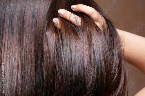 Fotografía A beautiful brunette woman is seen closeup, stroking fingers through straightened and conditioned glossy brown hair with room for copy