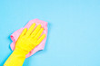 Hand in yellow gloves and microfiber rag cleaning blue background.